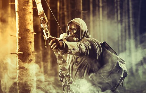 A male bow hunter wearing gas mask, draws back on his bow